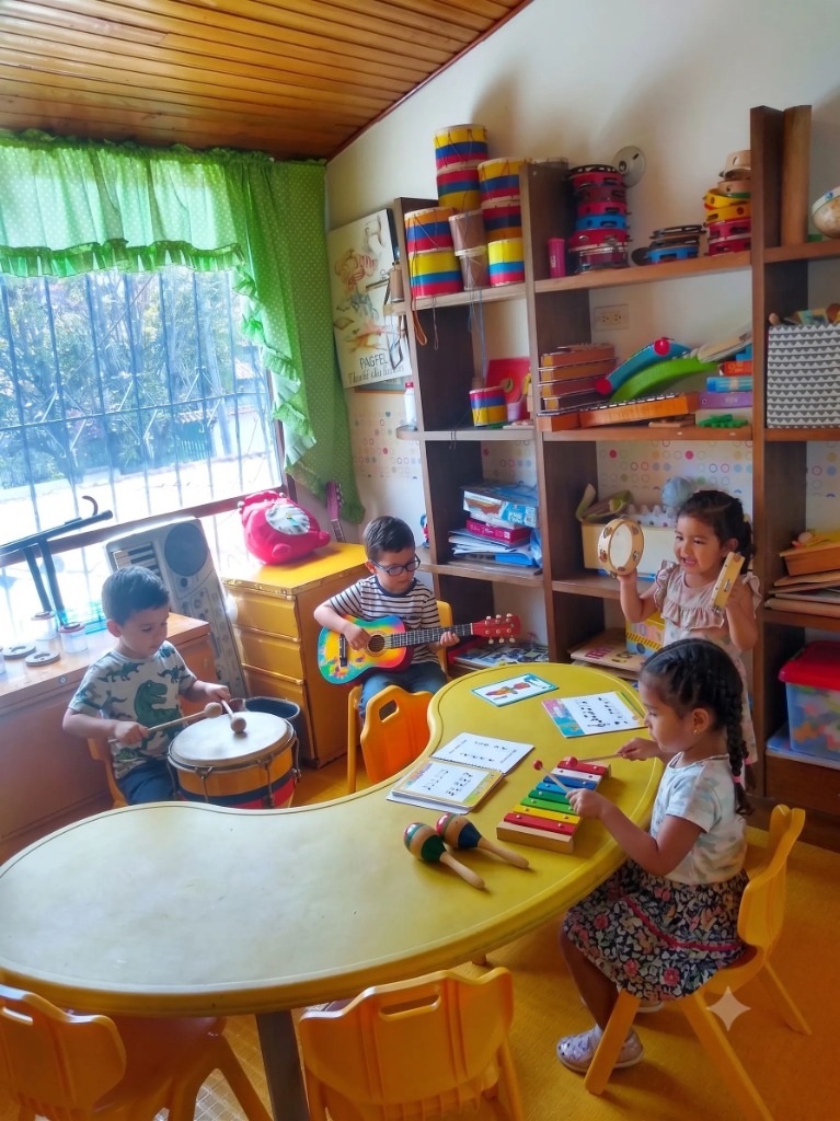 Niños sonriendo y tocando instrumentos como tambores, xilófonos y guitarras en el salón de música